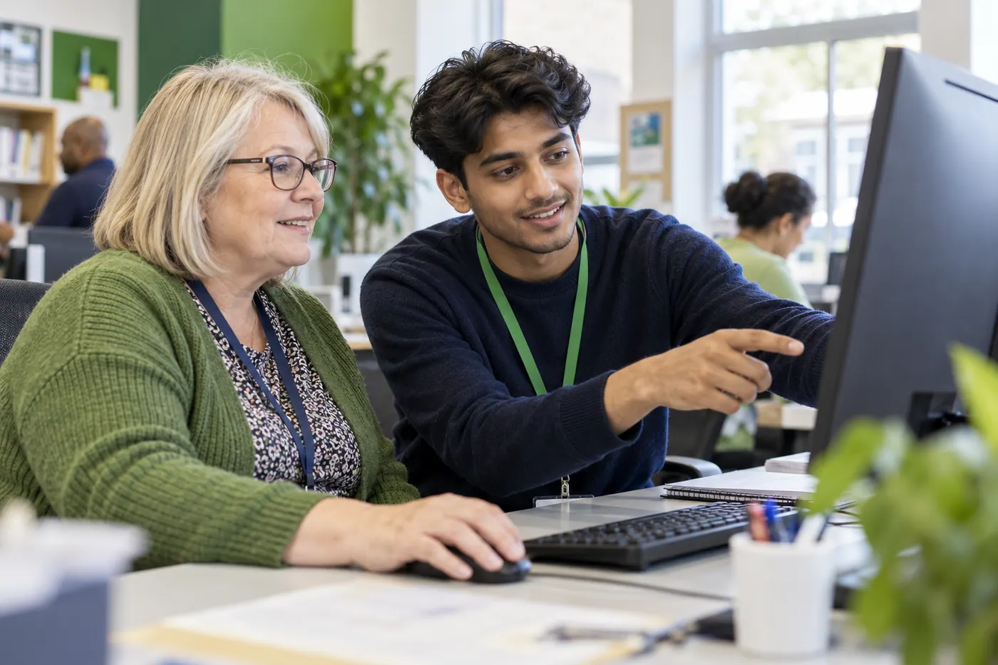 A digital-support apprentice helping a colleague use a desktop computer.