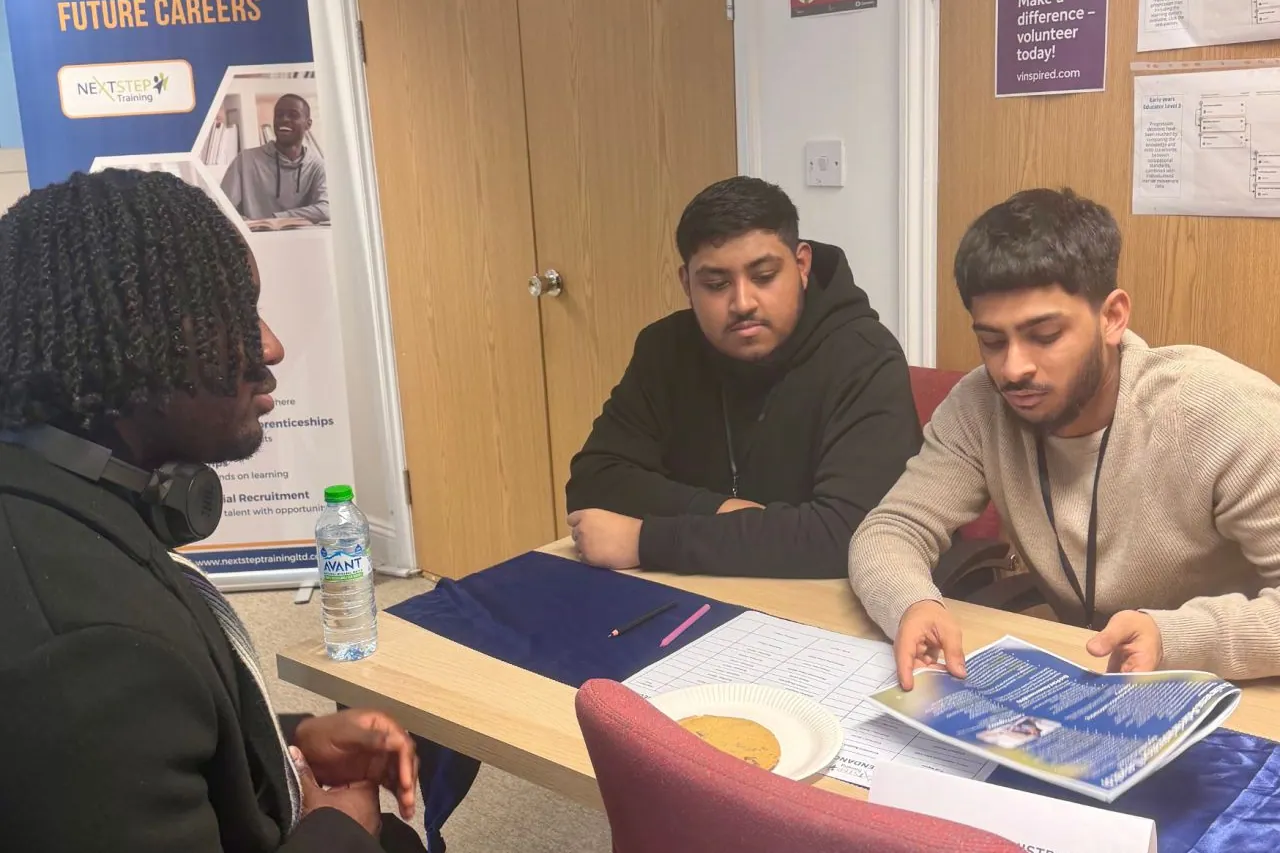 Three people discussing an apprenticeship programme brochure around a table.