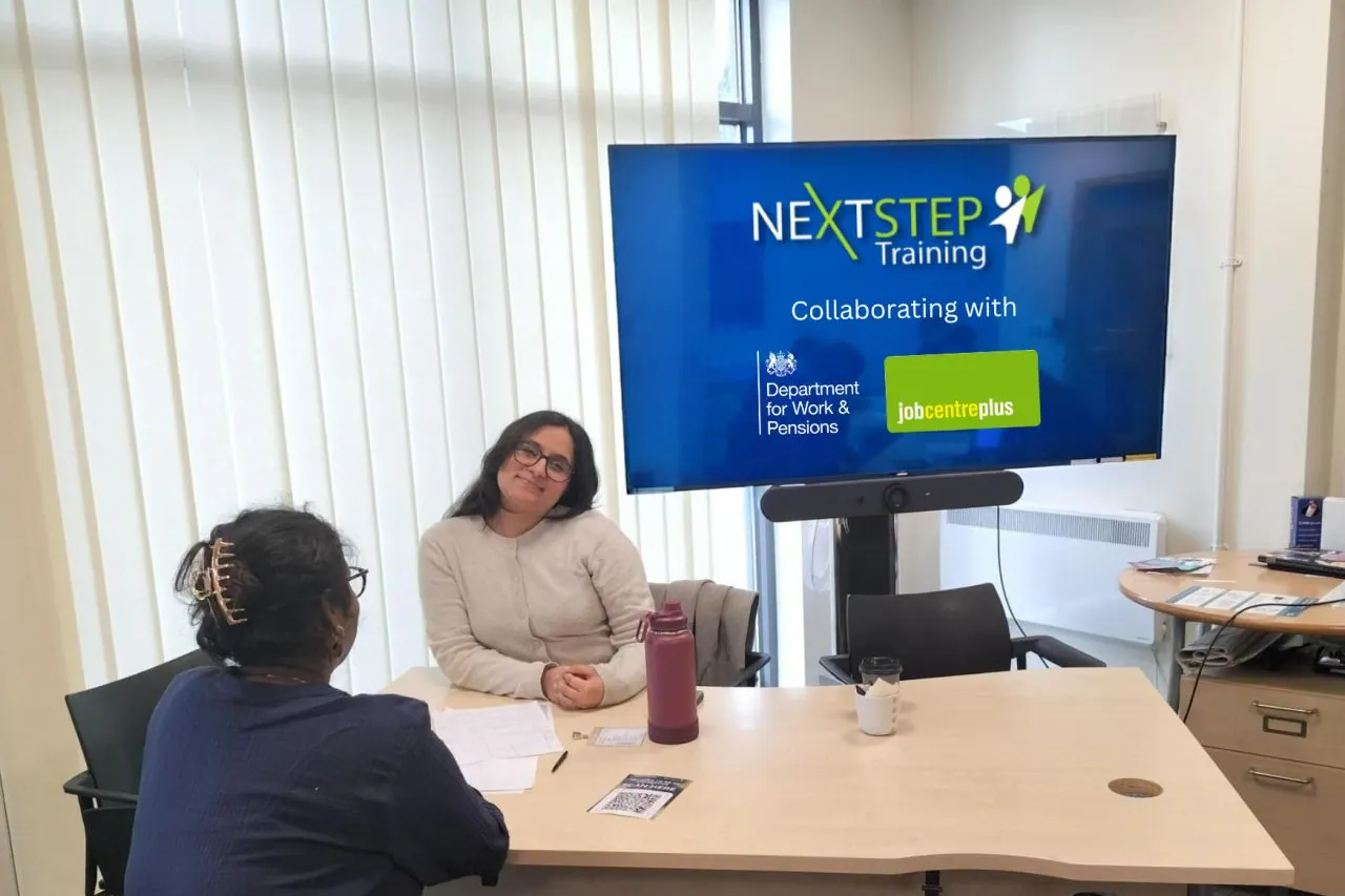 Two people meeting at a desk beside a screen showing NextStep’s collaboration with DWP and Jobcentre Plus.