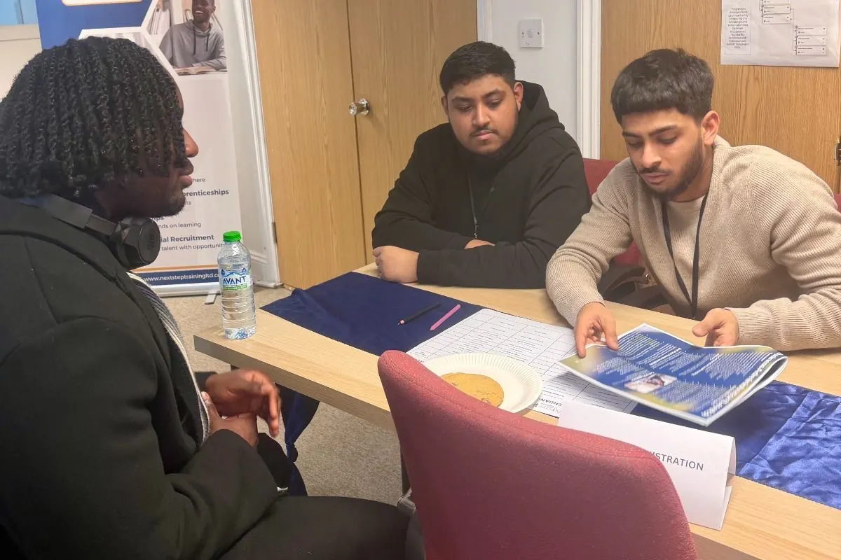 An adviser talking two candidates through programme information at a NextStep recruitment session.