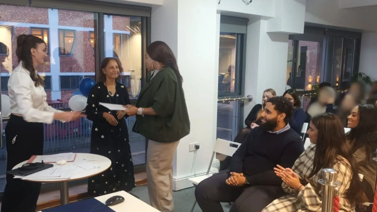 A certificate presentation at an apprenticeship ceremony, with the audience applauding.