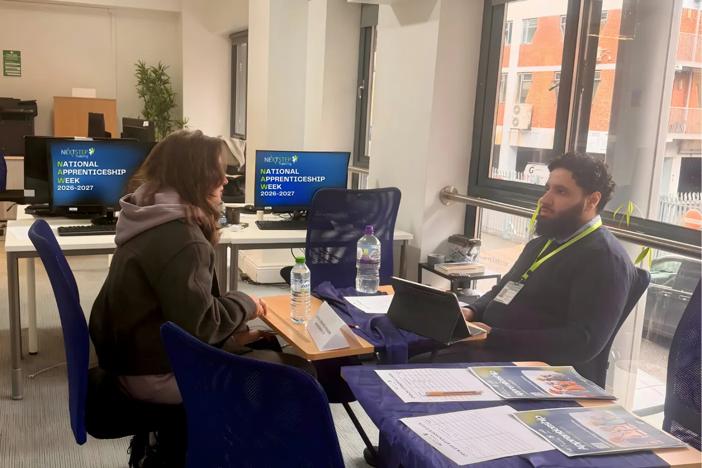 Two people discussing programme information across a desk at a recruitment and advice session.